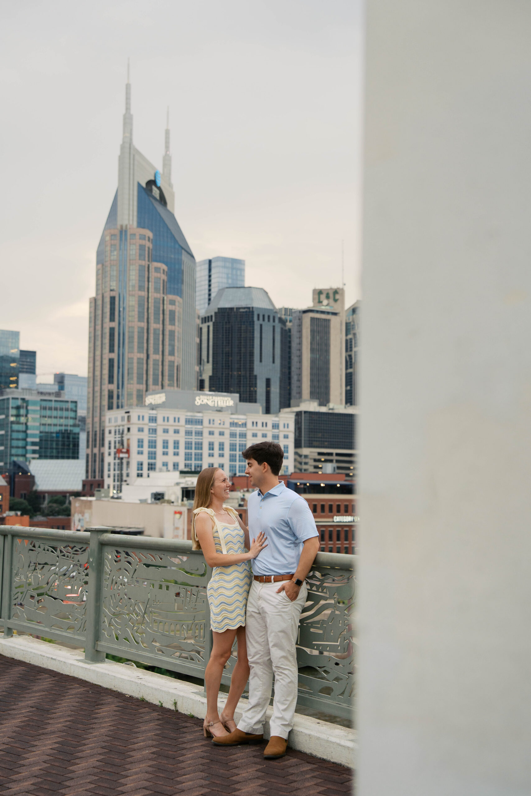 A couple holding onto each other smiling looking at each other during their engagement session on the pedestrian bridge in nashville Tennessee.