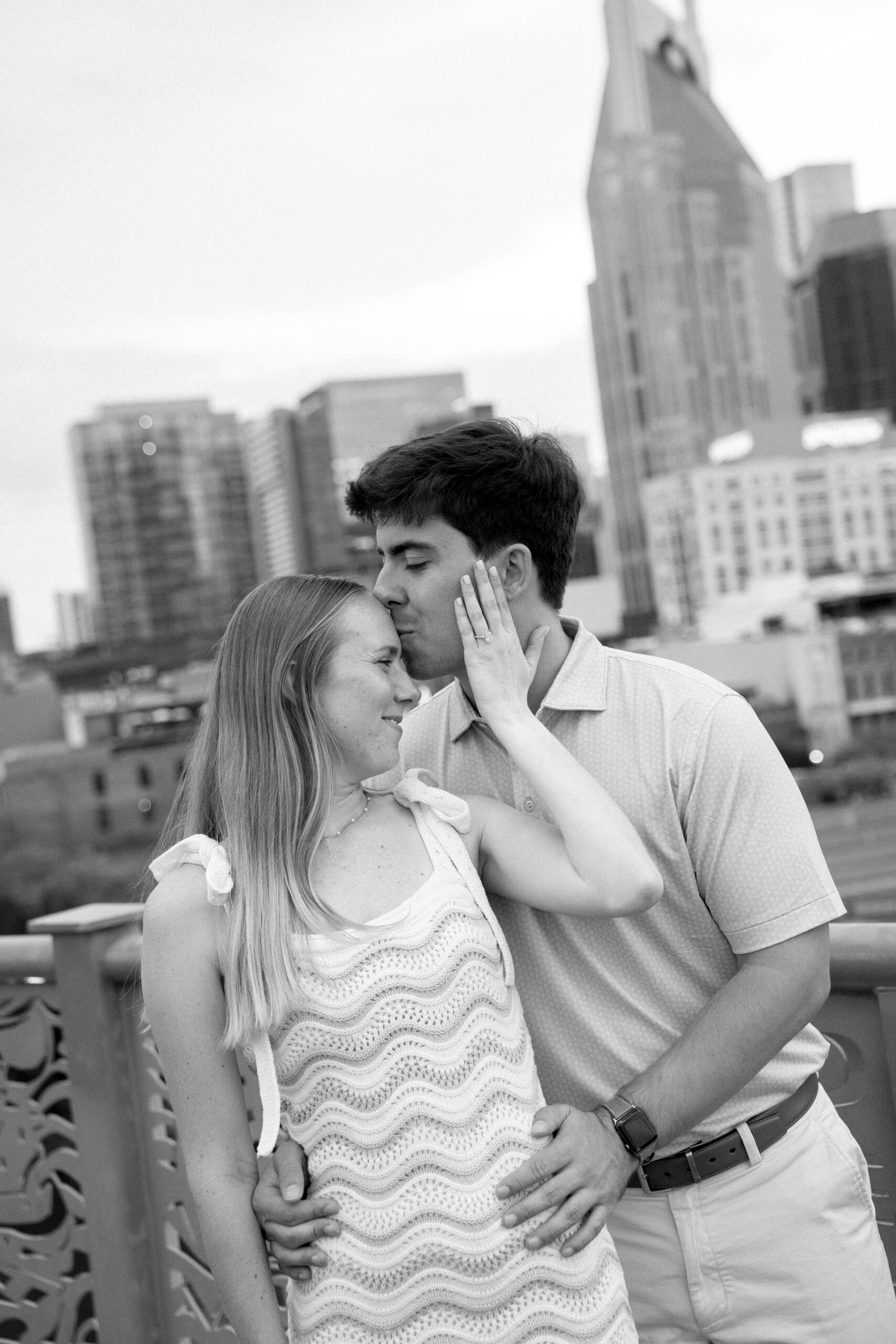 A man kissing the forehead of a woman during their engagement session on the pedestrian bridge in nashville Tennessee.