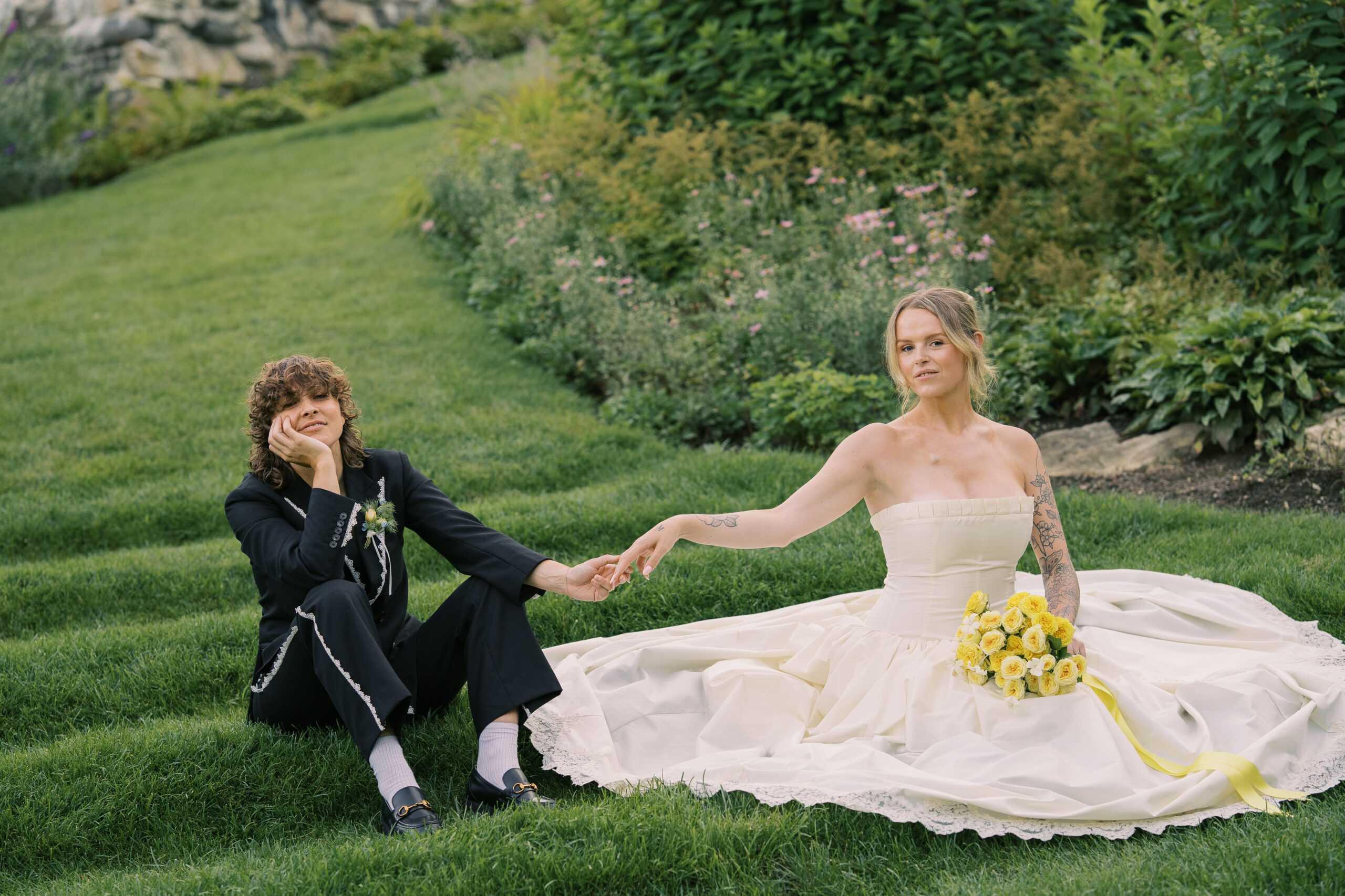 Two brides sitting on a greenery filled step at the mount wedding venue in Lenox massachusetts.