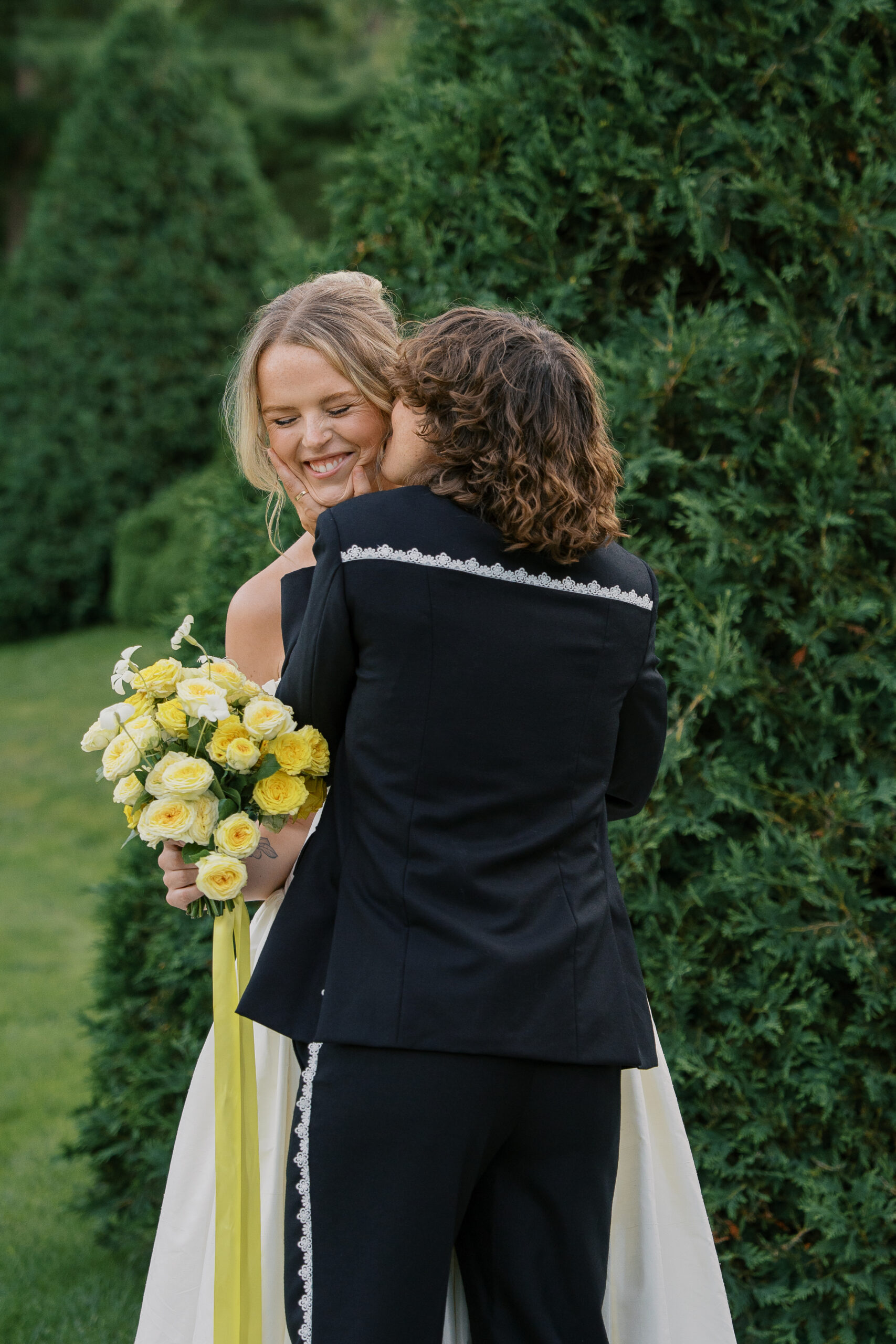 Two brides together on their wedding day at the mount in the Berkshires massachusetts kissing each other on the cheeks laughing.