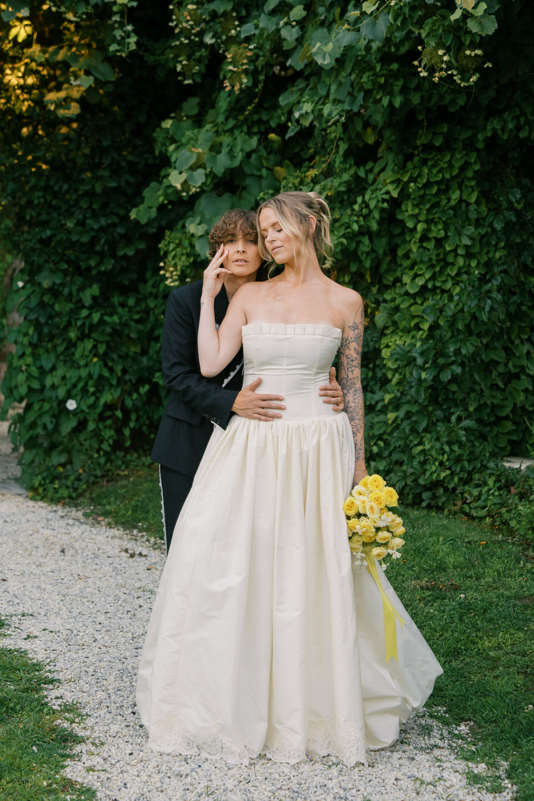Two brides on their wedding day holding each other with a bouquet of yellow roses for a portrait during golden hour.