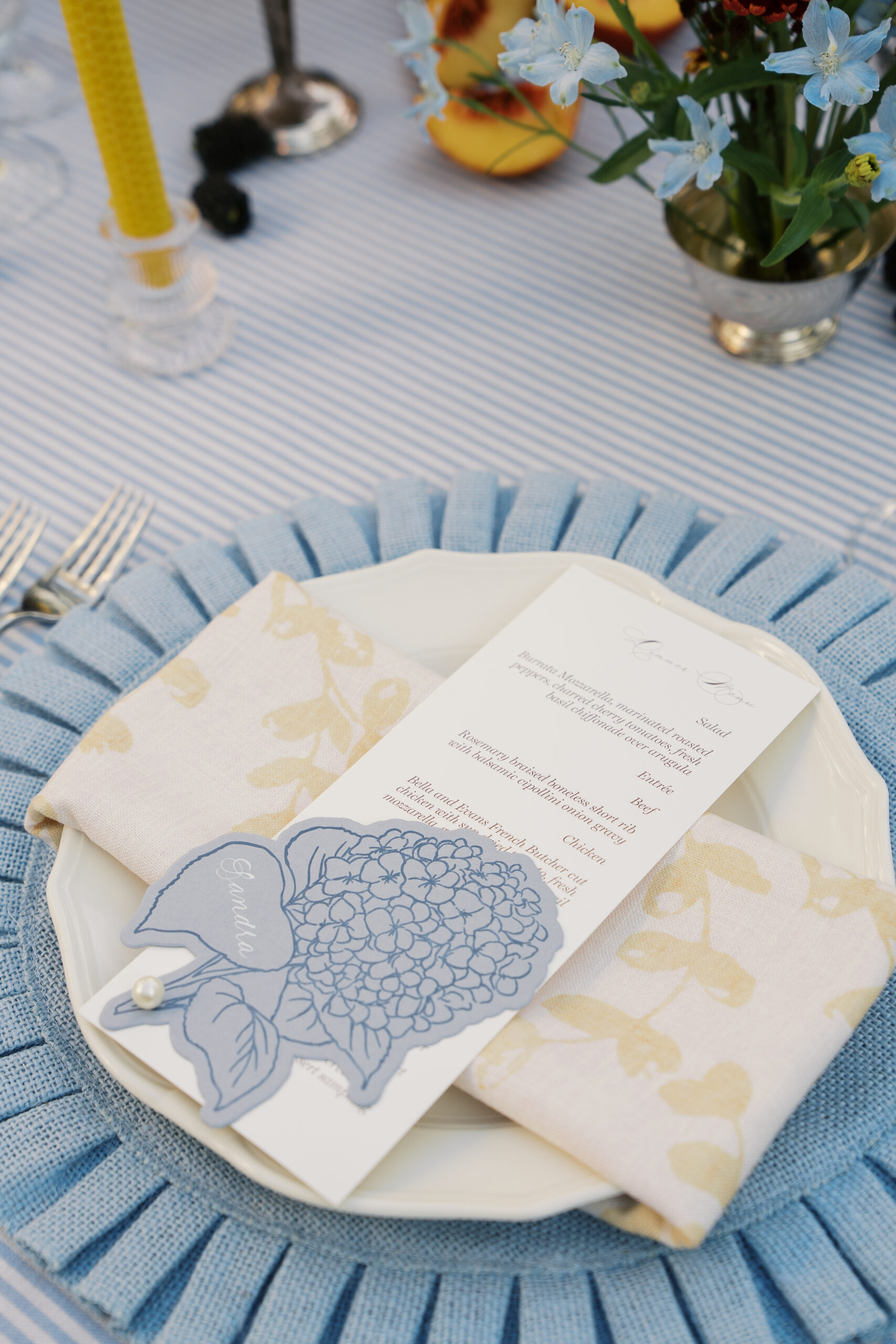 A place setting with a blue charger and a menu with a hydrangea.