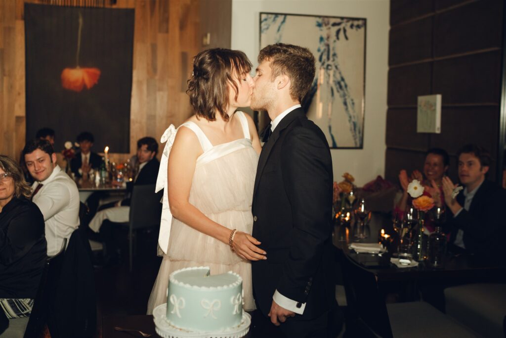 newly married couple kissing after cutting their wedding cake 