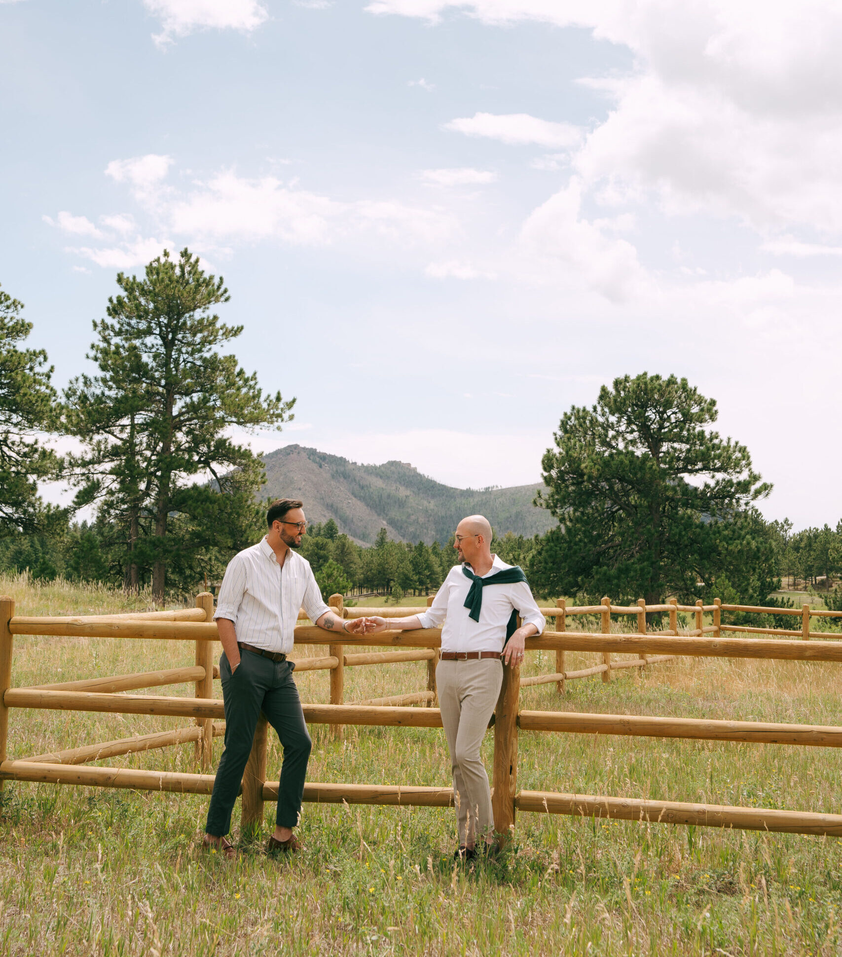 lgbtqia+ couple leaned up against a fence in colorado