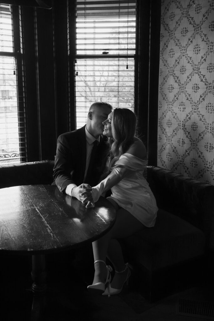 black and white couple kissing on the cheek at a bar next to the window 