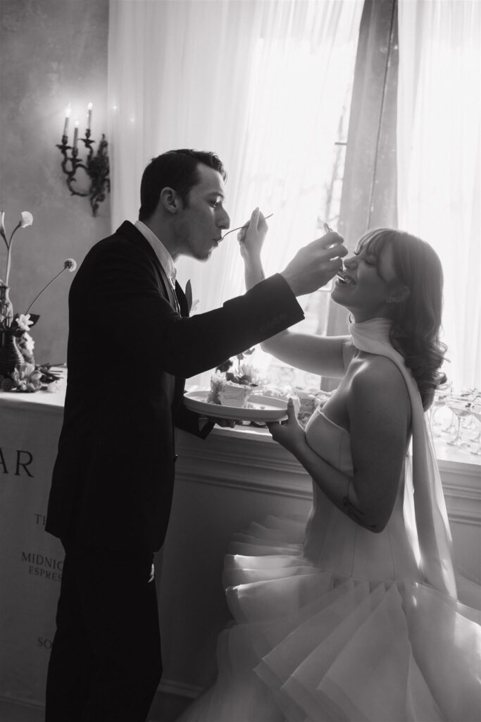 black and white photo of wedding couple feeding each other cake 