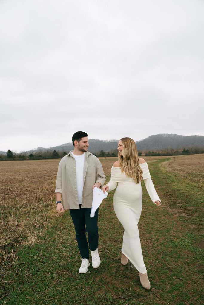 happy couple walking and holding baby onesie 