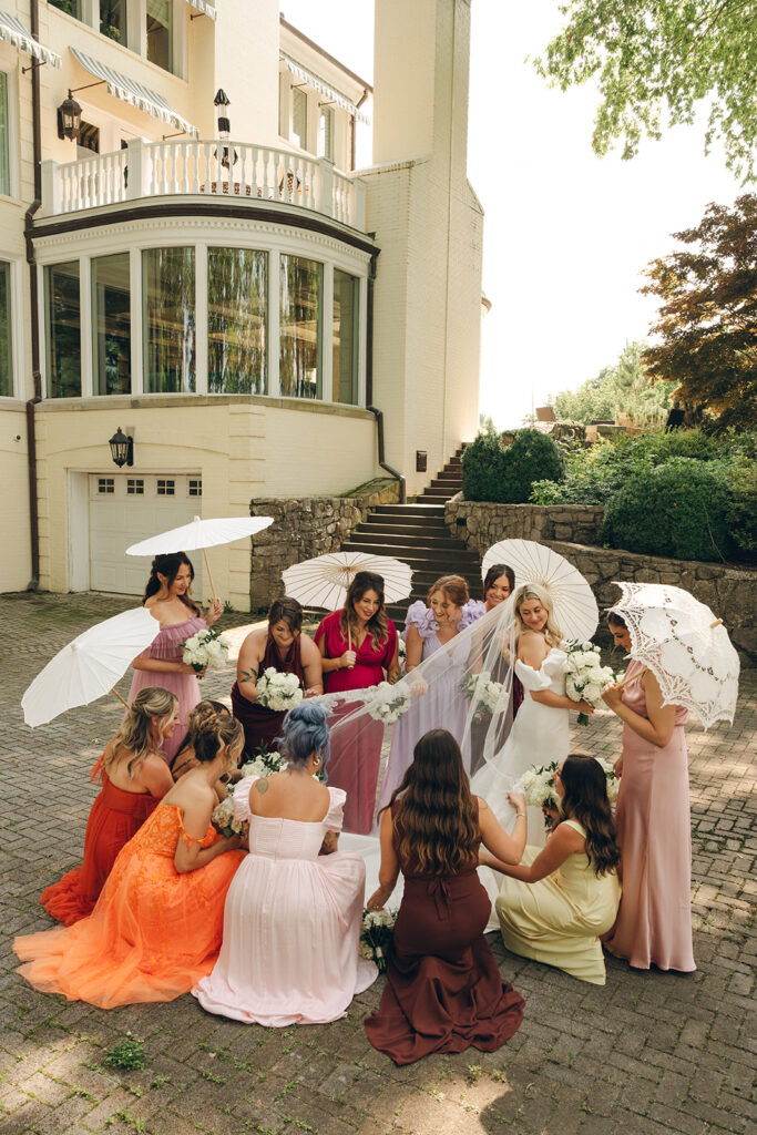 colorful bridesmaids adjusting brides dress while holding parasols 