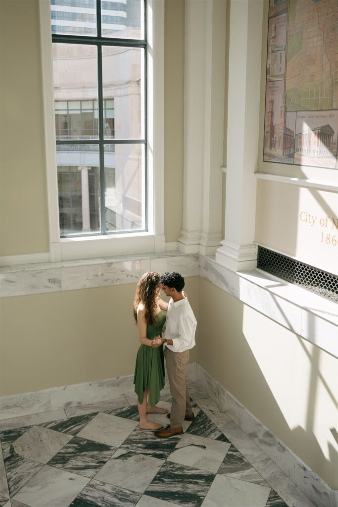 engaged couple dancing under a window with lots of natural light and marble floors 