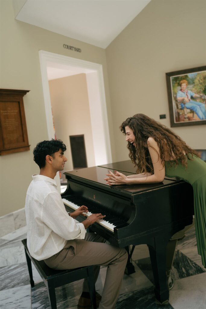woman in a green dress smiling at boyfriend playing a grand piano 