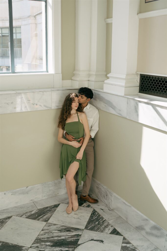 man kissing woman on the head from behind at a public library with marble floors 