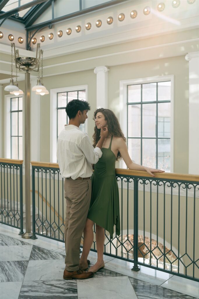 woman in green dress leaning against railing with partner cupping her face at a public library with natural lighting 