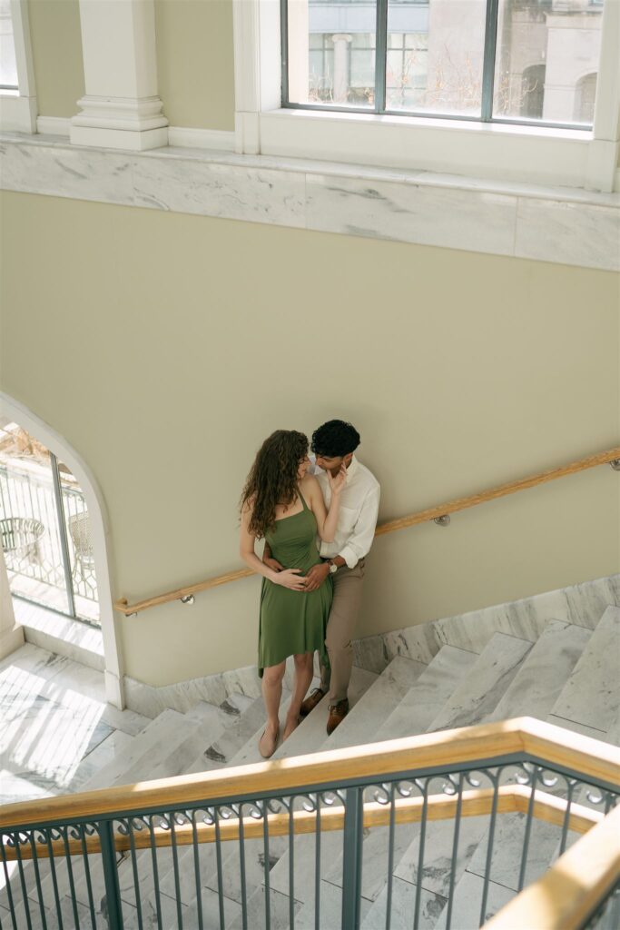 couple hugging on the marble stairs leaning against the railing 